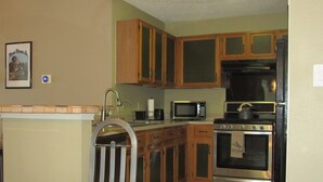 Una cocina compacta con armarios de madera, microondas, horno y una mesa de comedor de vidrio.