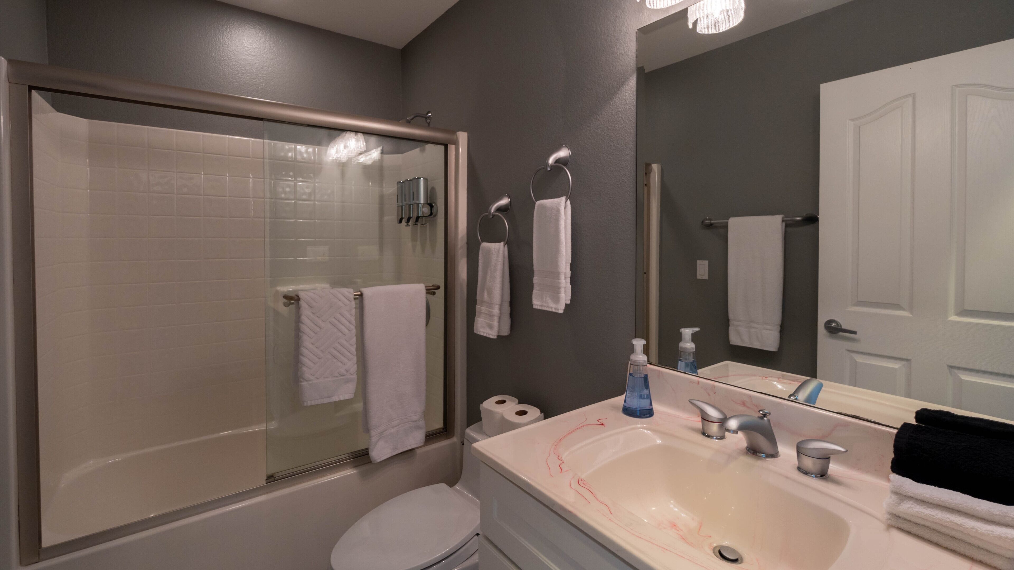 Un bany amb una cabina de dutxa de vidre, un vàter blanc, un lavabo amb mirall i diverses tovellas blanques.