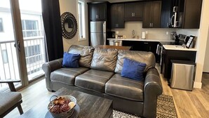 Een modern appartement met een leren bank, een eettafel, een keuken met donkere kastjes en een kleine koelkast.