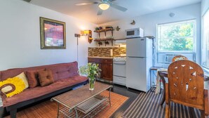 Un espace de vie compact comprenant un canapé, une table à manger, un coin cuisine avec réfrigérateur et cuisinière, et un ventilateur de plafond.
