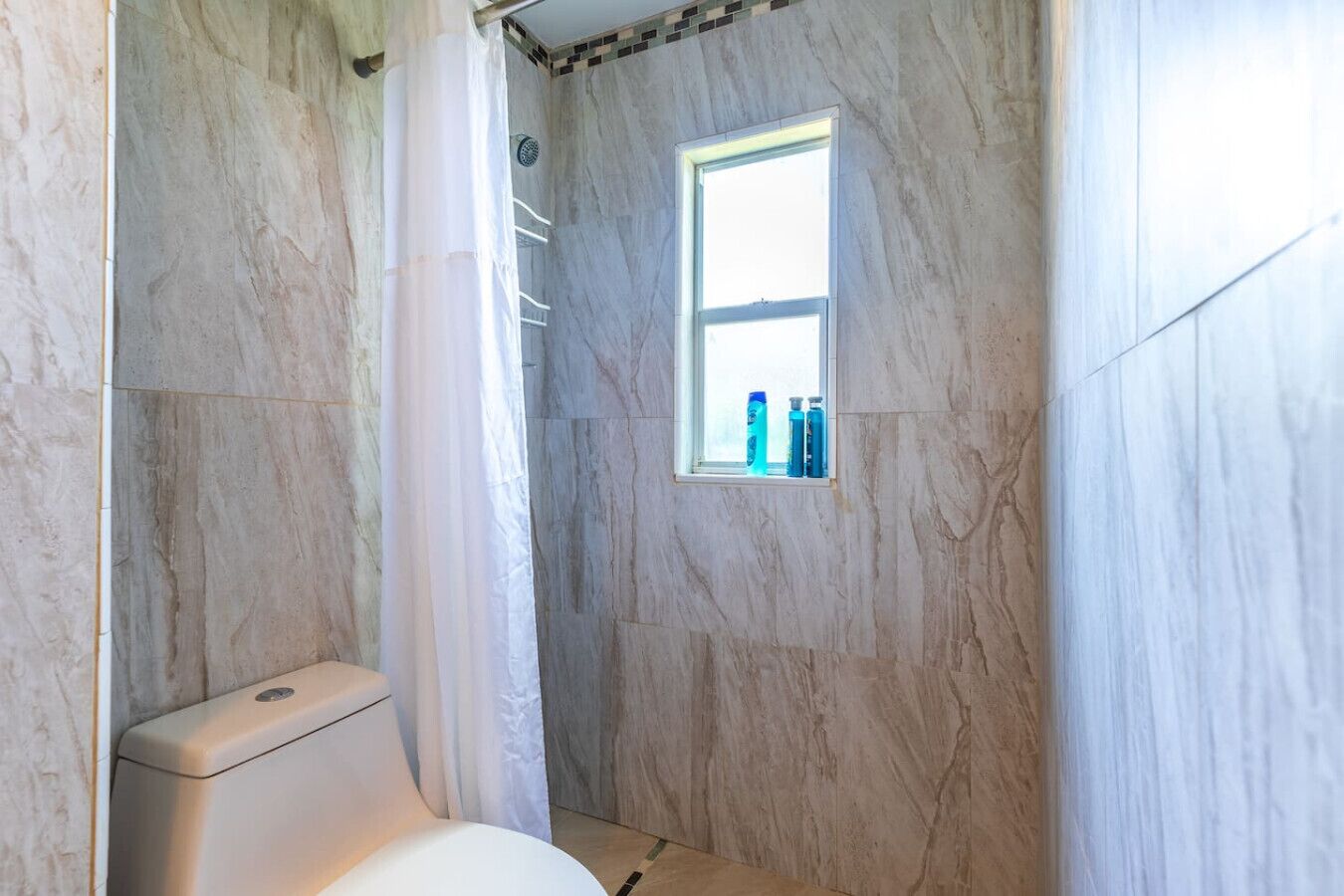 Un baño con inodoro, ducha y ventana con artículos de aseo.