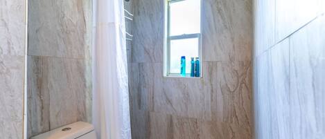 Un baño con inodoro, ducha y ventana con artículos de aseo.