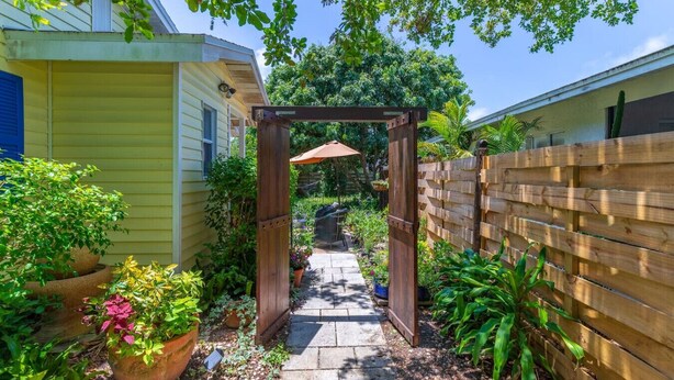 Un étroit sentier mène à une arche en bois, qui est entourée de plantes en pot et d’une clôture en bois.
