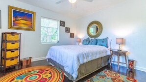 Une chambre à coucher avec un lit, un ventilateur de plafond, une fenêtre, un miroir et un tapis coloré.