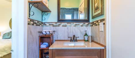 Un baño con lavamanos de mármol, armarios de madera, un perchero y un espejo.