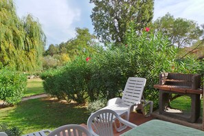 A patio area with a grill, two white plastic chairs, and a table.