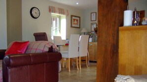 A cozy living room with a leather sofa, a dining area with a table and chairs, and a kitchen area with wooden cabinets. - The Oaks - Award Winning Barn Conversion In Hope Village Near To Castleton (Hope)