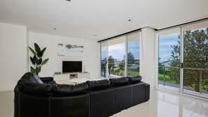 Una sala de estar moderna con un sofá de cuero negro, un televisor de pantalla plana y un ventanal con vistas al exterior.