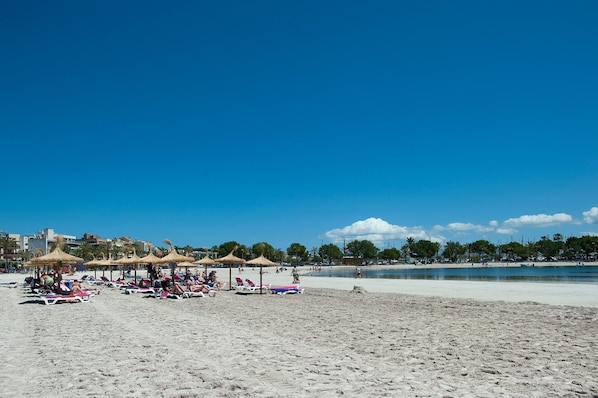 A beach with sun loungers and umbrellas, a clear sky, and a calm sea.