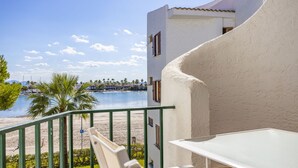 Un balcón con vista a una playa y al mar, una mesa blanca y una silla.