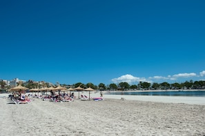 A beach with sun loungers and umbrellas, a clear sky, and a calm sea.