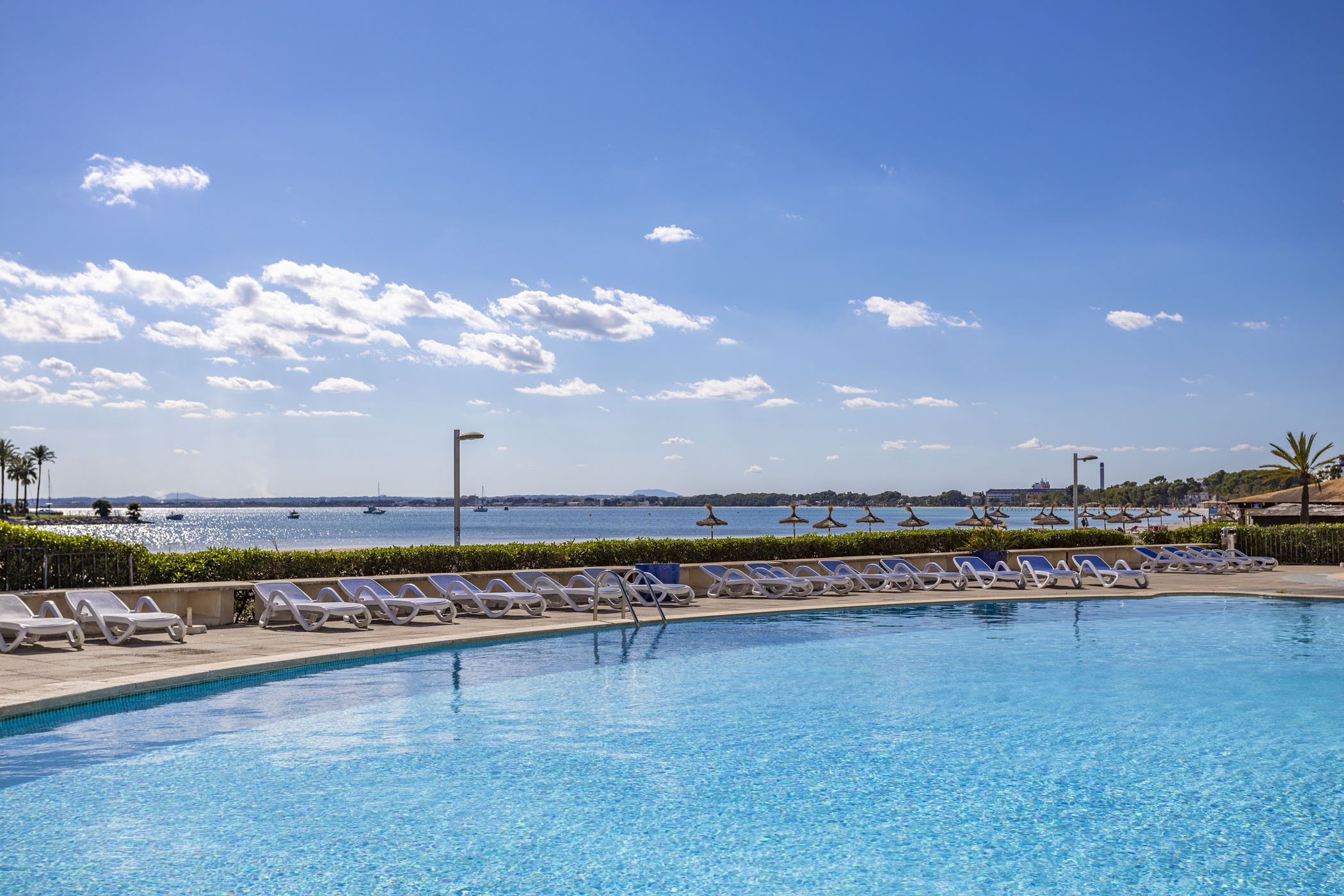 A swimming pool with lounge chairs and umbrellas, a clear sky, and a view of the sea.
