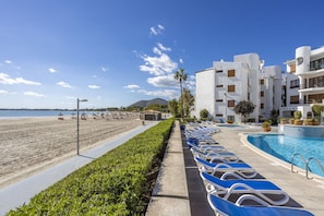 A resort with a pool, beach, and white buildings with balconies.
