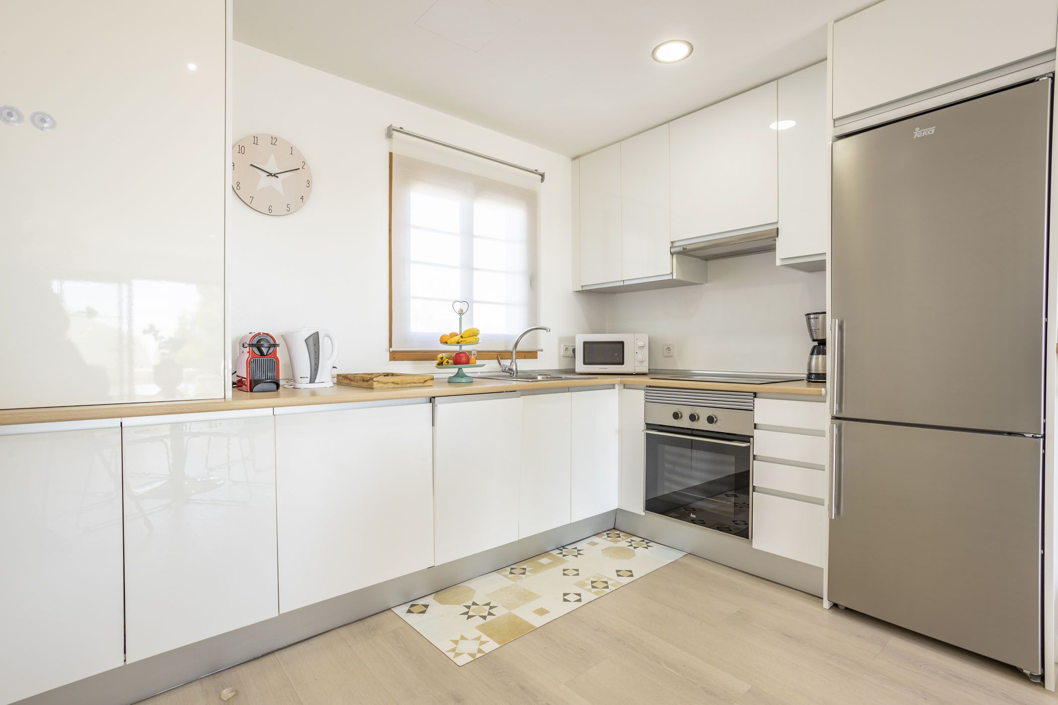 A modern kitchen with white cabinets, a stainless steel refrigerator, a microwave, and an oven.