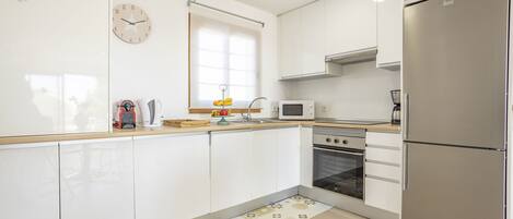 A modern kitchen with white cabinets, a stainless steel refrigerator, a microwave, and an oven.