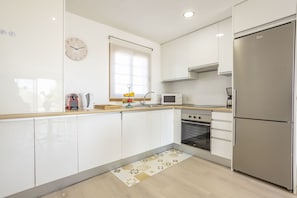 A modern kitchen with white cabinets, a stainless steel refrigerator, a microwave, and an oven.