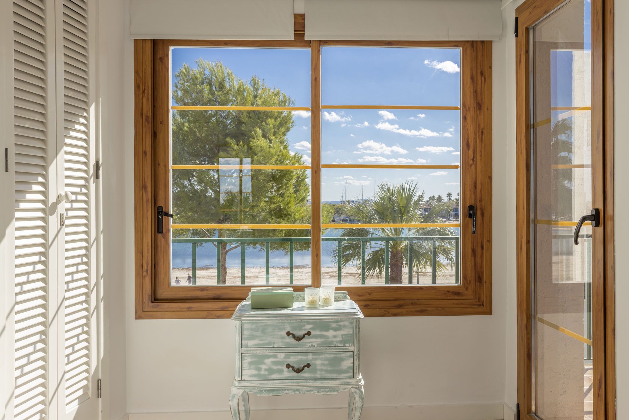 A room with a large window offering a view of a beach and palm trees.