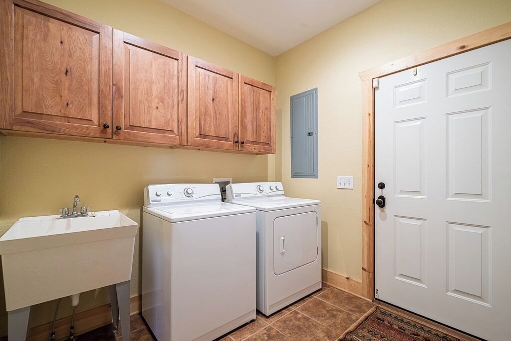 A laundry room with a sink, two washing machines, and wooden cabinets.