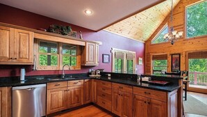 A spacious kitchen with wooden cabinets, a stainless steel dishwasher, and a black countertop.