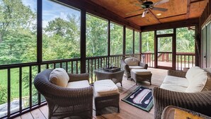 A covered porch with wicker furniture, large windows, and a ceiling fan.