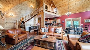 A spacious living area with leather sofas, a wooden staircase, and a kitchen in the background.