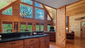 A cabin interior with a wooden interior, large windows, a kitchen area, and a cozy seating area.