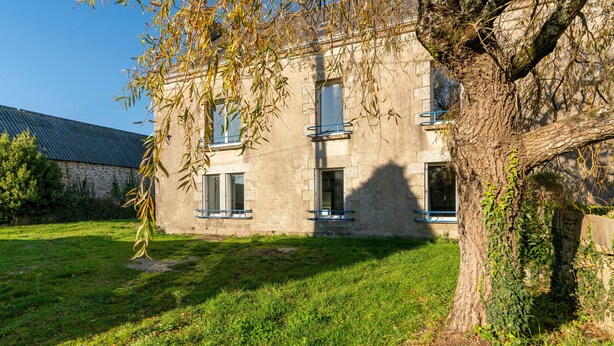 Un bâtiment en pierre avec trois fenêtres et un arbre devant.