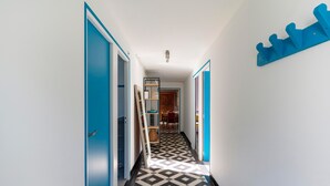 Un couloir avec un sol à carreaux, des portes bleues et un porte-manteau bleu fixé au mur.