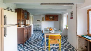 Une cuisine avec un sol carrelé, des meubles de rangement en bois, une table à manger avec des chaises et un réfrigérateur.