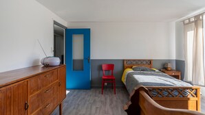 Une chambre à coucher avec un lit en bois, une chaise rouge, une porte bleue et une commode en bois.