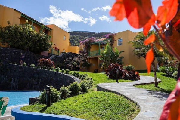 A resort with a swimming pool, lush landscaping, and yellow buildings.