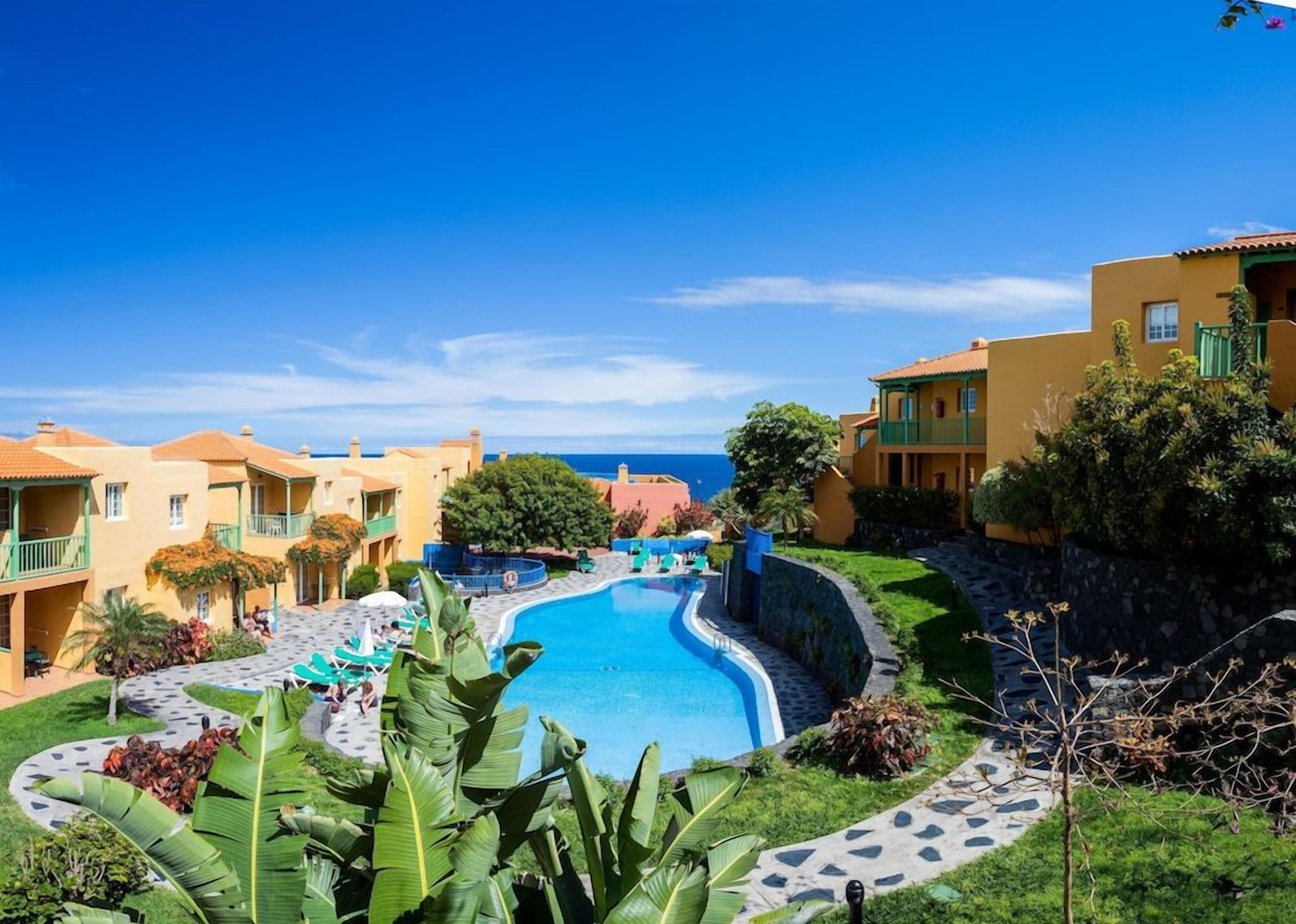 Een resort met een zwembad, meerdere gebouwen en een helder uitzicht op de zee.