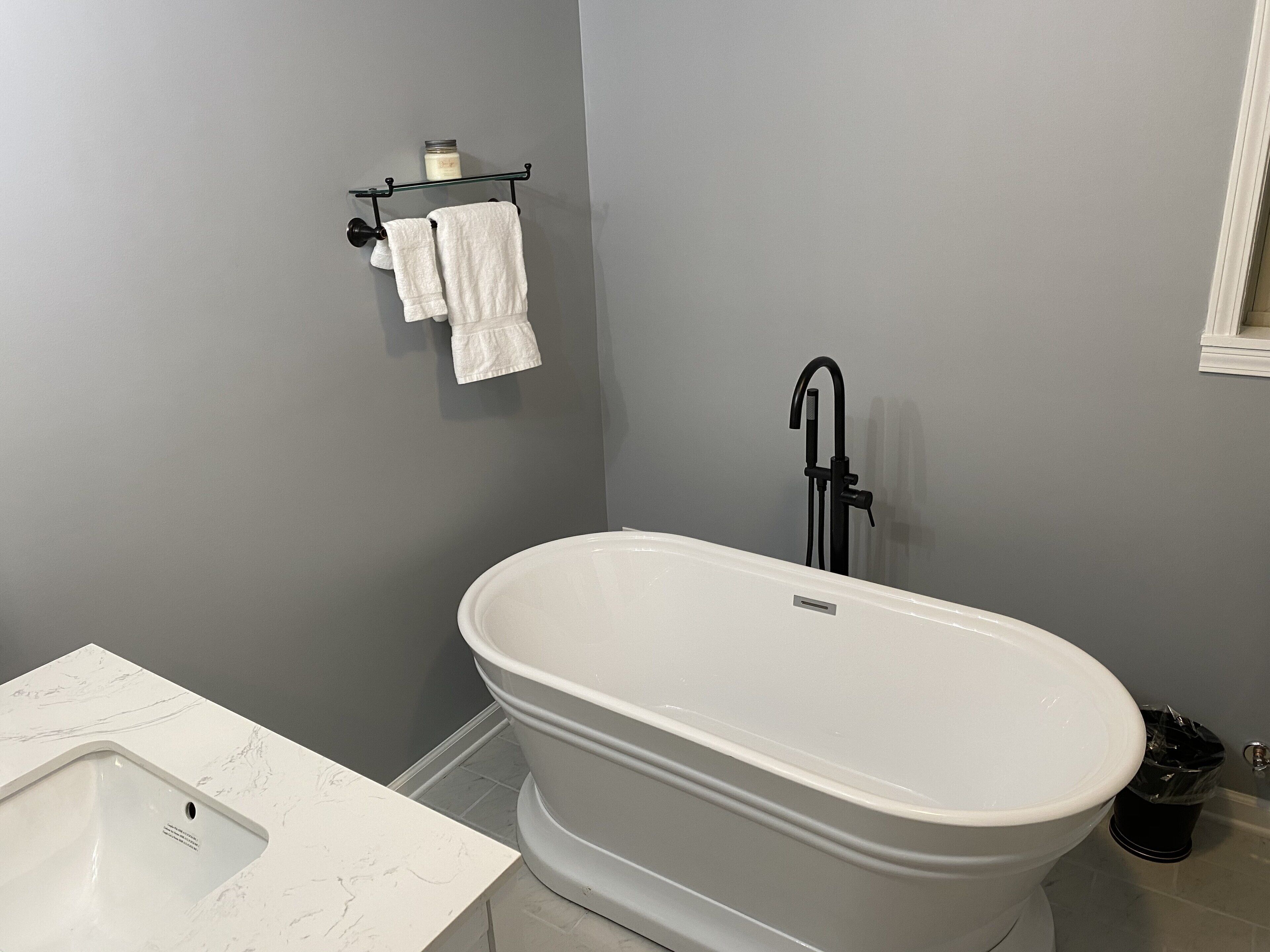 Une salle de bain avec une baignoire îlot, un lavabo blanc doté d’un plan-vasque imitant le marbre, et un porte-serviettes avec deux serviettes blanches.