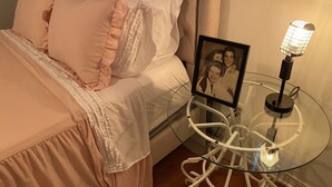 Una camera da letto con un letto, cuscini, un comodino con una cornice e una lampada.