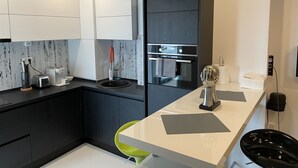 A modern kitchen with dark cabinets, a white countertop, a built-in oven, and a green chair. - Fancy Westpark 2 Residence Lake View W7 (Bucharest)
