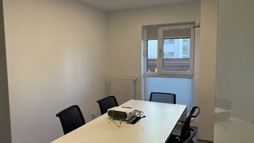 A conference room with a white table, four black chairs, a projector, and a window with blinds.