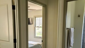 Un couloir mène à une chambre à coucher qui comprend un lit, une fenêtre et une salle de bain avec un porte-serviettes.