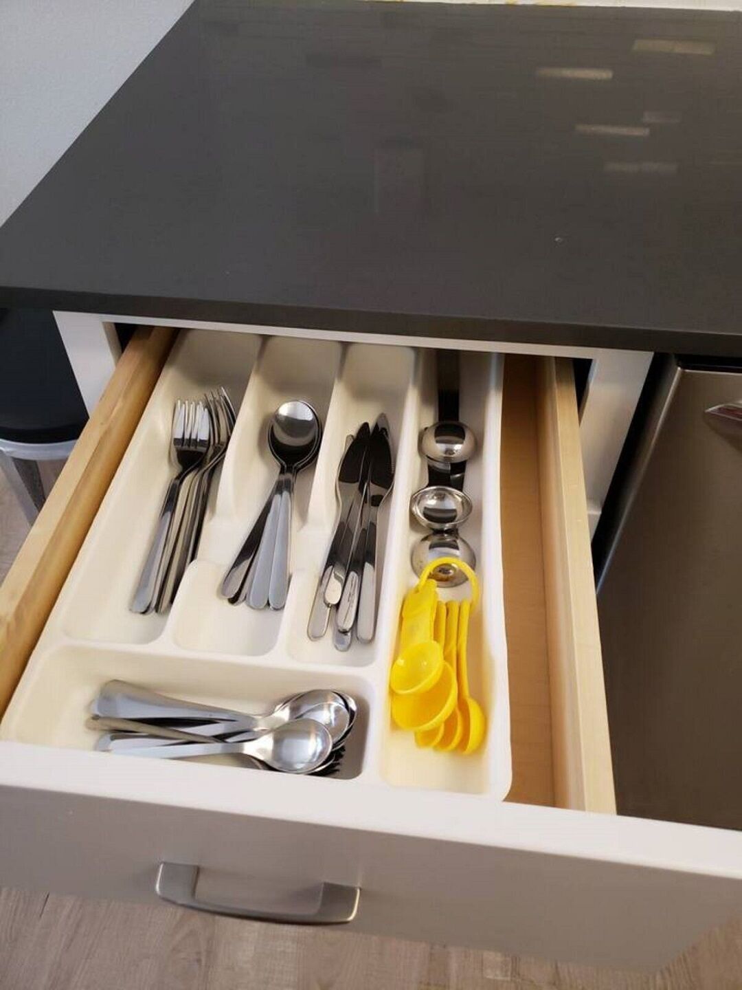A drawer with neatly organized silverware and yellow measuring cups.