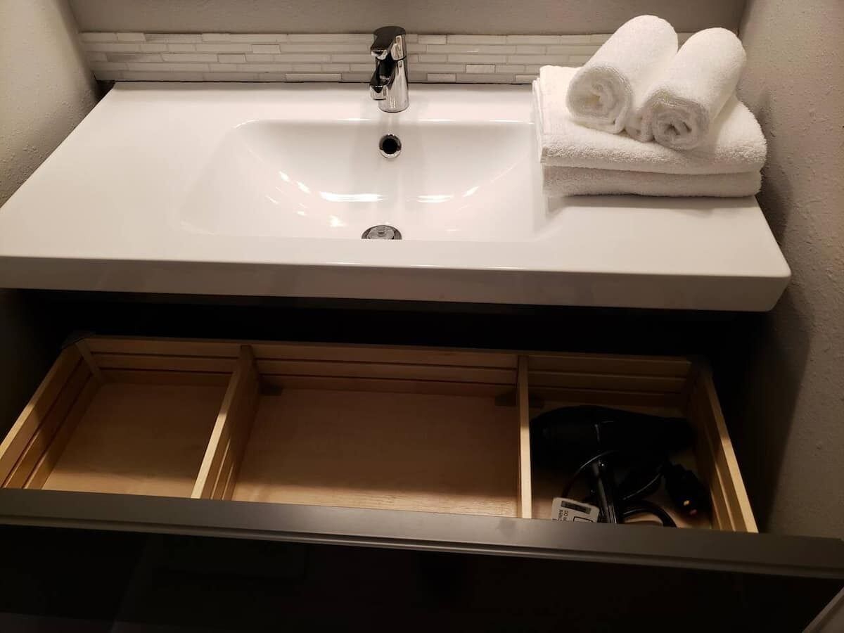 Un baño con un lavamanos blanco, un perchero y un cajón de madera.