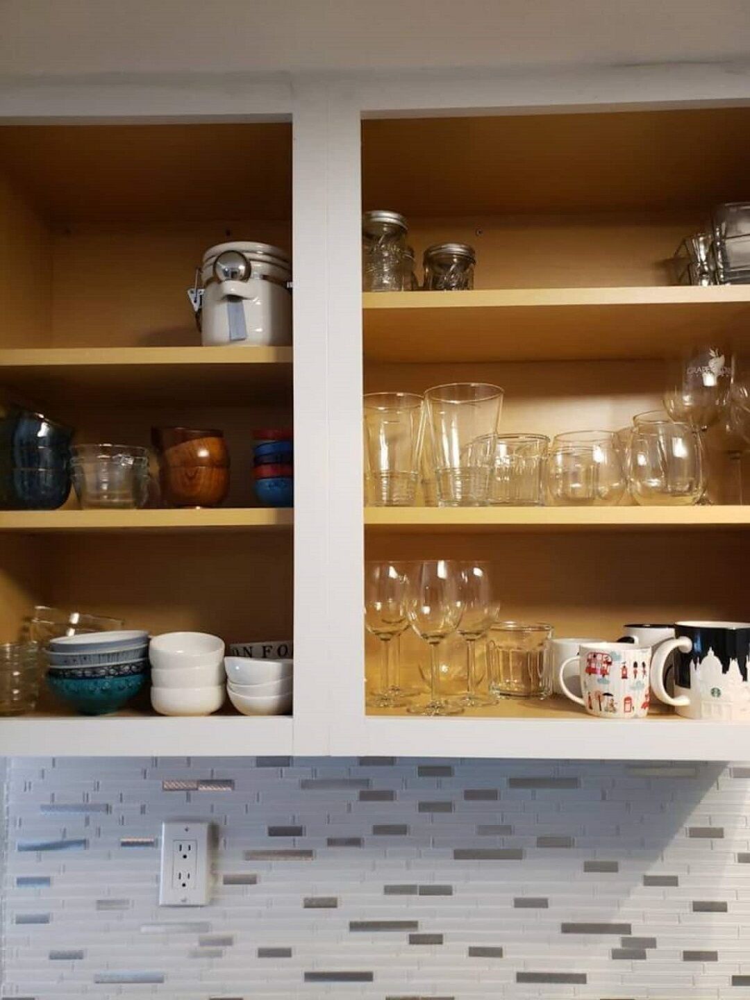 A kitchen with wooden shelves holding various glassware, including wine glasses and cups.