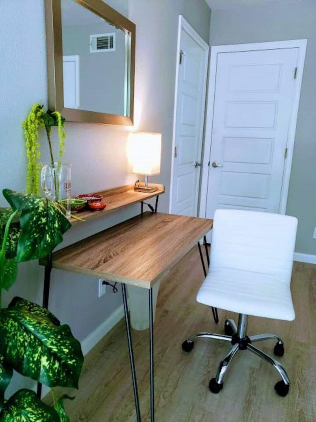 A small office space with a wooden desk, a white office chair, a mirror, and a potted plant.