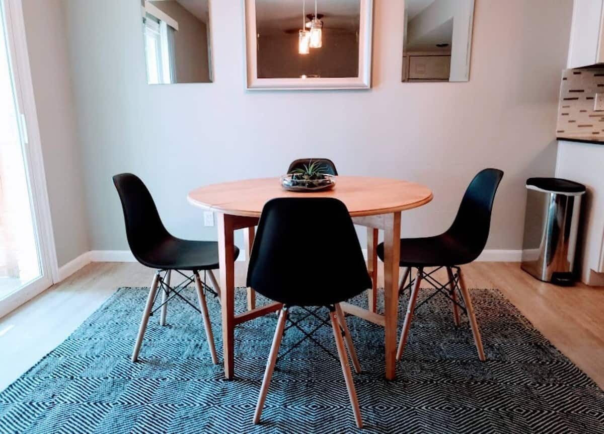 Un coin repas avec une table ronde, quatre chaises noires, une petite plante posée sur la table et un luminaire suspendu au-dessus.