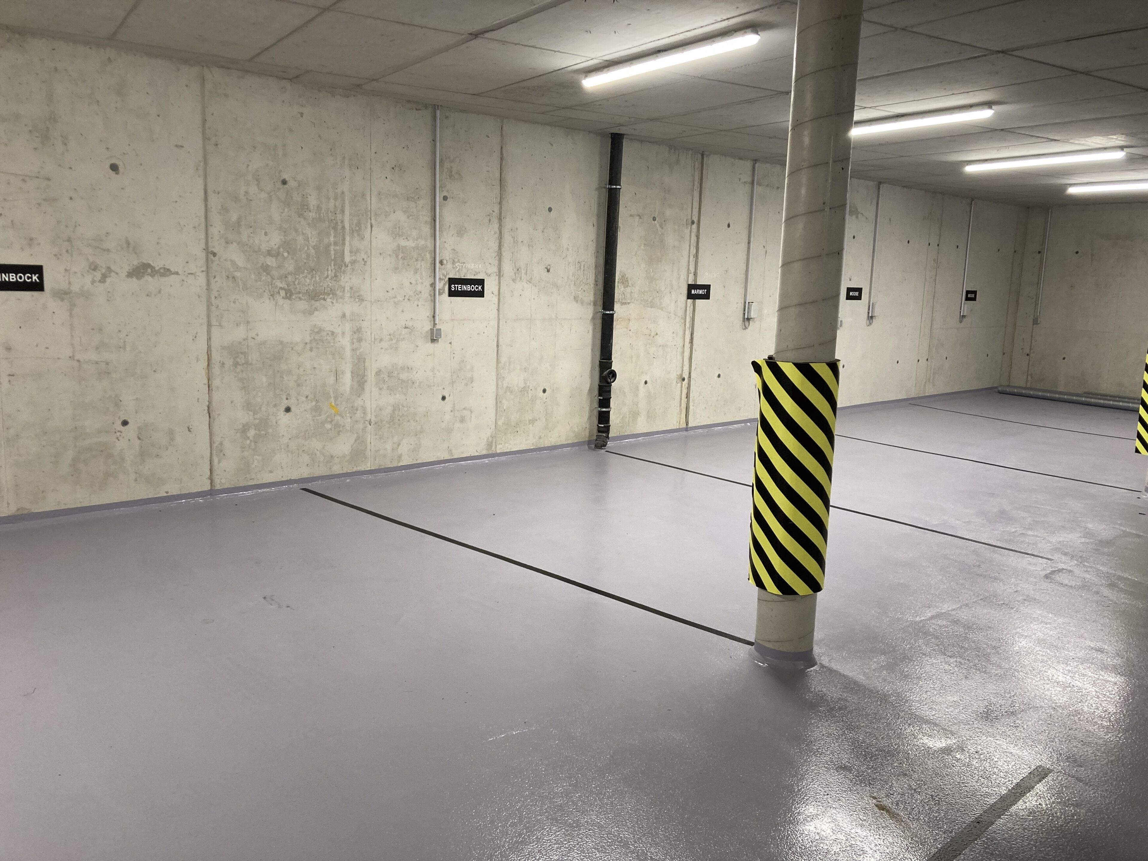 Un estacionamiento con paredes de concreto, espacios delimitados y bolardos con rayas amarillas.