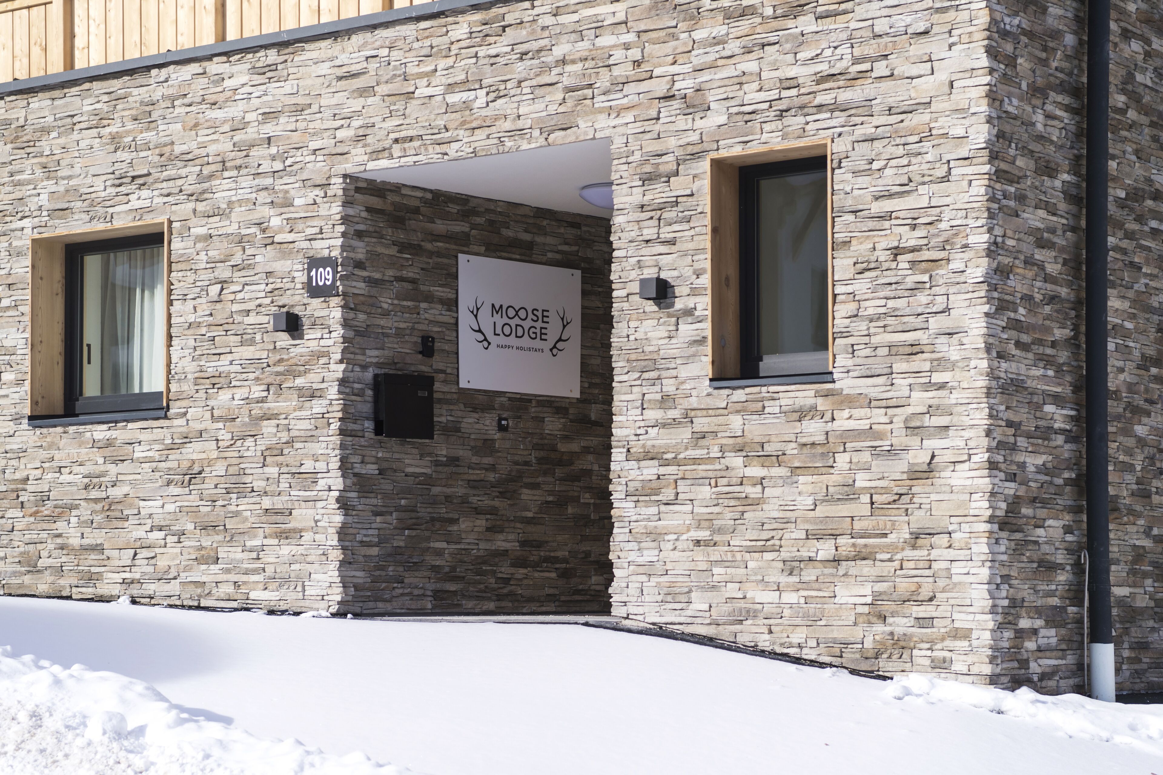 Ein Gebäude mit einer Steinauffahrt, einem Schild mit der Aufschrift 'Moose Lodge Happy Holidays' und einem mit Schnee bedeckten Gelände.