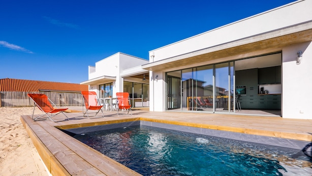 Een modern huis met een zwembad, zitplaatsen buiten en een keuken die zichtbaar is door glazen deuren.