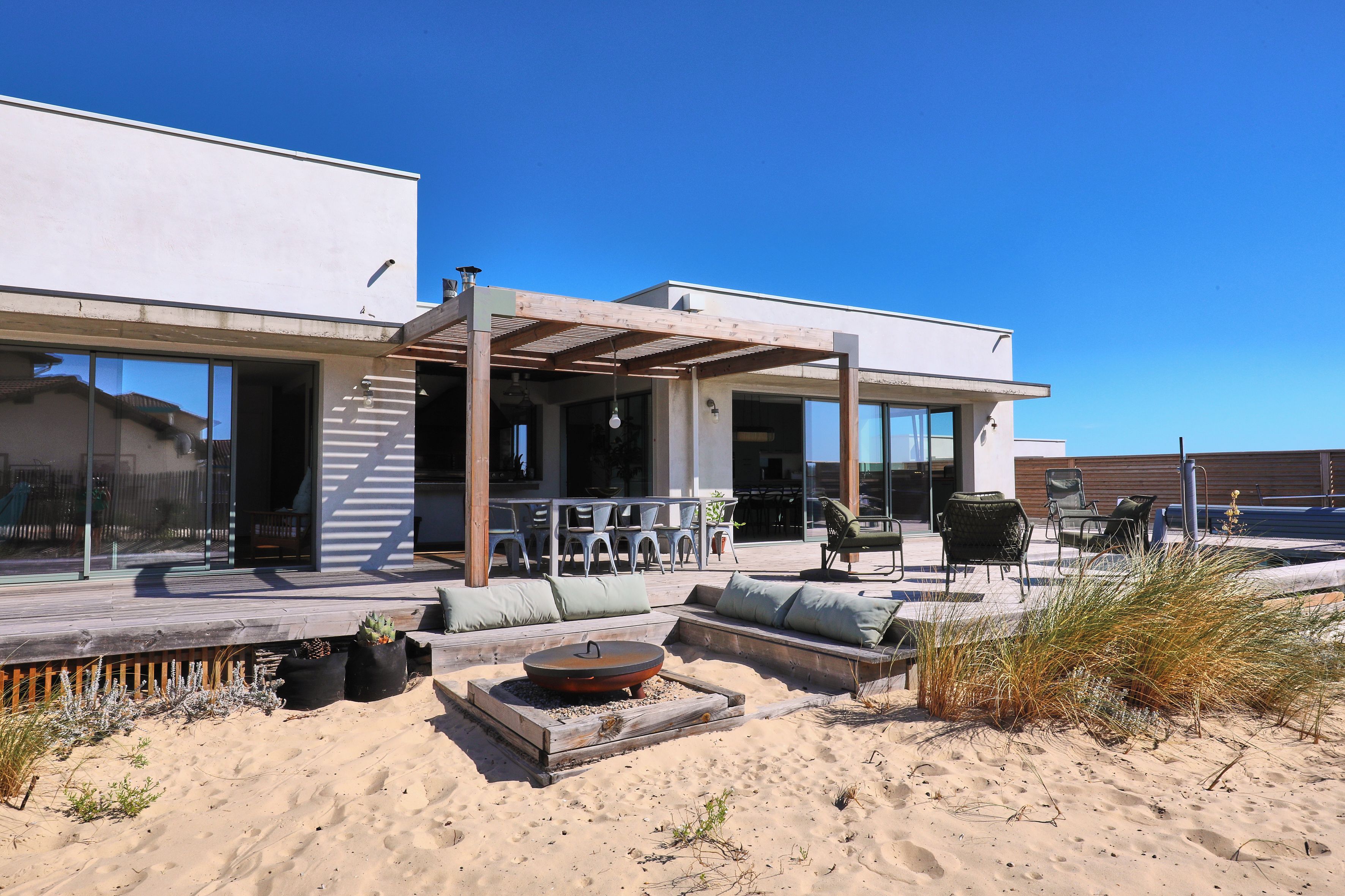 A modern outdoor patio with seating, a fire pit, and a covered area with chairs and tables.