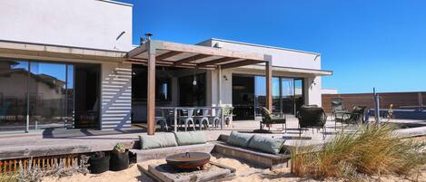 A modern outdoor patio with seating, a fire pit, and a covered area with chairs and tables.