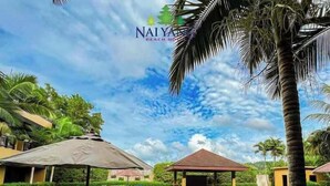 A swimming pool with lounge chairs and umbrellas, surrounded by greenery and a clear sky. - Naiyang Beach Hotel (Sa Khu)