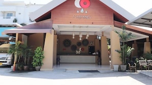 The exterior of Naiyang Beach Hotel with a modern design, featuring a prominent logo, a reception area with a counter, and potted plants around the entrance. - Naiyang Beach Hotel (Sa Khu)