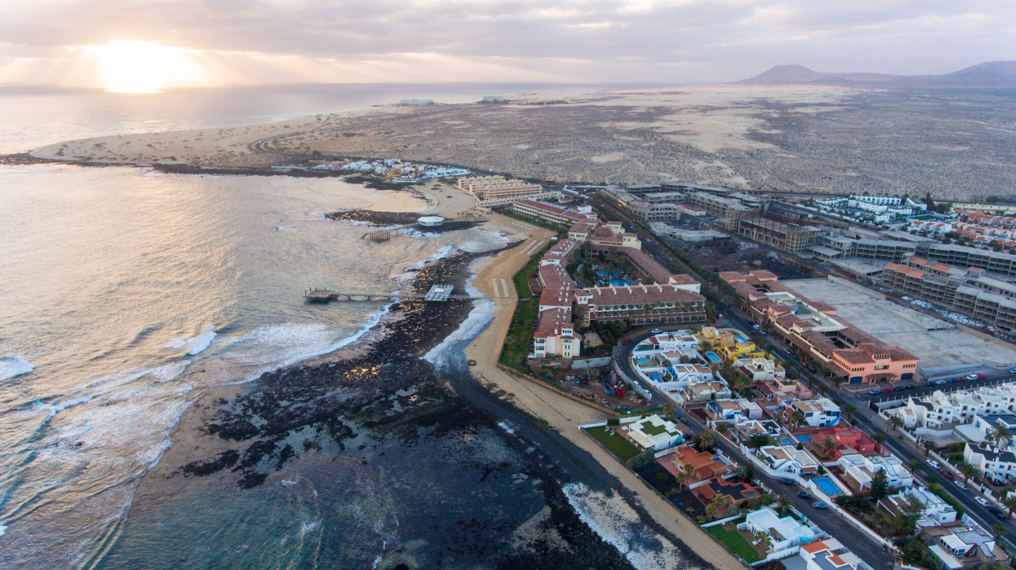 Vue aérienne d’une station balnéaire avec des villas en bord de mer, un port de plaisance et un grand complexe hôtelier.